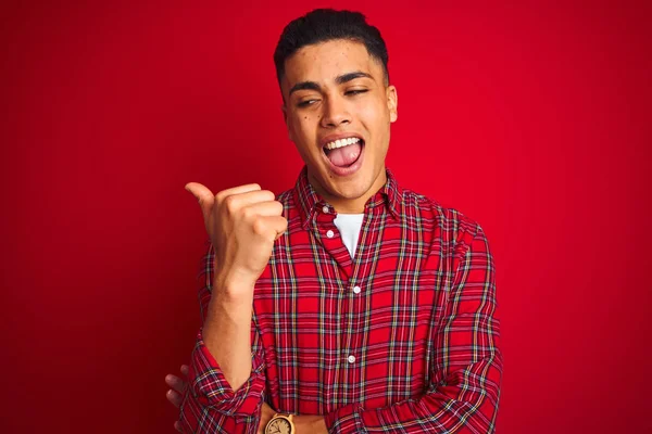 年轻的巴西男子穿着衬衫站在孤立的红色背景微笑与快乐的脸看 并指着一边竖起大拇指 — 图库照片