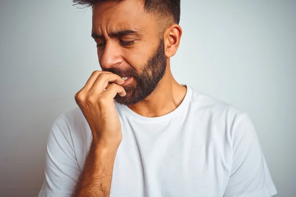 孤立した白い背景の上に立つTシャツを着た若いインド人男性は 口を噛む爪に手を当て ストレスと緊張しているように見えます 不安の問題 — ストック写真