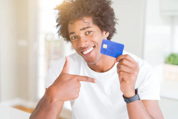 African American man holding credit card with surprise face pointing finger to himself
