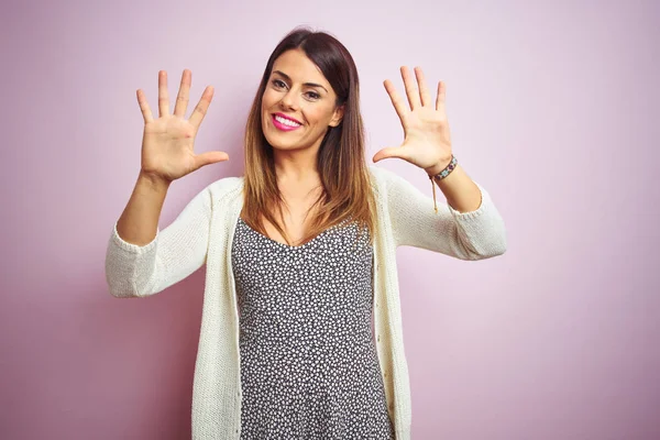Genç güzel kadın pembe izole arka plan üzerinde duran gösteren ve parmakları ile işaret on numara emin ve mutlu gülümserken.