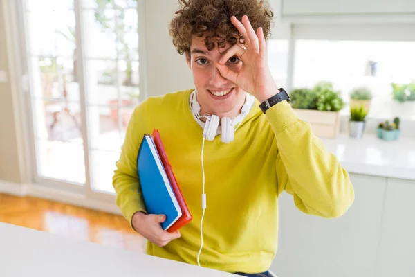 年轻的学生男子戴着耳机 拿着笔记本 开心的脸微笑着做好标志 手对眼睛透过手指看 — 图库照片