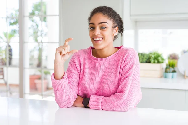 カジュアルなピンクのセーターを着たアフロヘアの美しいアフリカ系アメリカ人女性は 指を見て カメラで小さなサイズのサインをやって手で自信を持ってジェスチャー 測定コンセプト — ストック写真