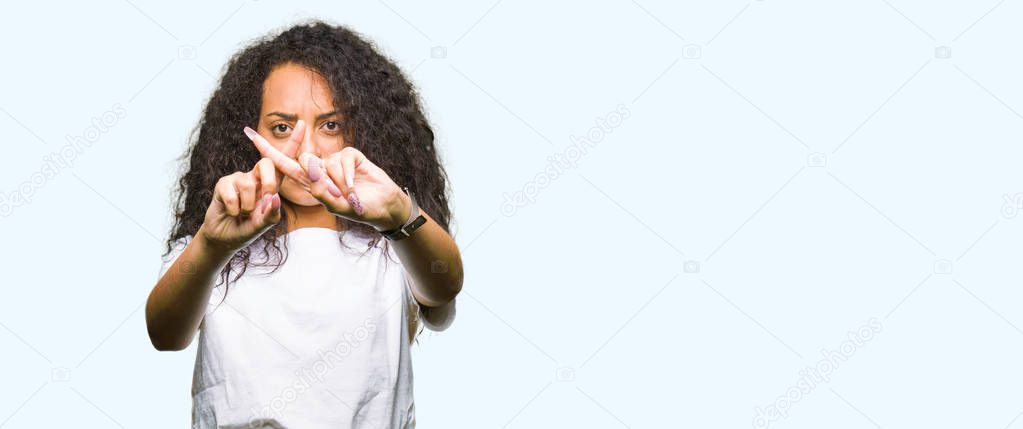 Young beautiful girl with curly hair wearing casual white t-shirt Rejection expression crossing fingers doing negative sign