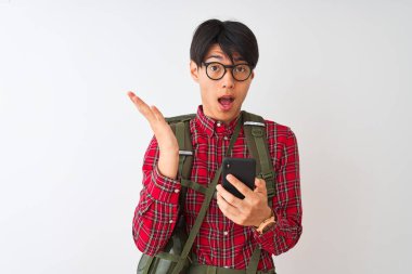 Izole beyaz arka plan üzerinde akıllı telefon kullanarak kantin giyen Çinli yürüyüşçü adam çok mutlu ve heyecanlı, kazanan ifade büyük bir gülümseme ile çığlık zafer kutluyor ve ellerini kaldırdı