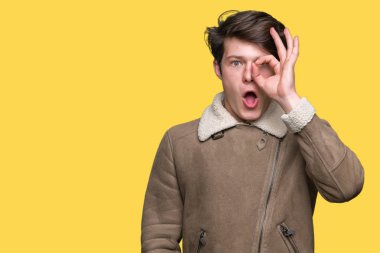 Sürpriz yüz, göz parmaklarının arasından seyir ile ok jest yapıyor izole arka plan üzerinde kış ceket giyen genç yakışıklı adam şok. İmansız ifade.