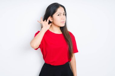 Izole arka plan üzerinde kırmızı t-shirt giyen güzel esmer kadın söylenti veya dedikodu bir işitme dinlerken kulak üzerinde el ile gülümseyerek. Sağırlık kavramı.