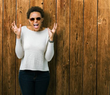 Arka plan deli kutluyor güzel genç Afro-Amerikan kadın üzerinde güneş gözlüğü takıyor izole ve crazy arms ile başarı için kaldırdı ve heyecanlı çığlık gözler kapalı. Kazanan kavramı