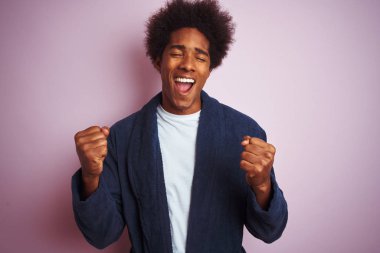 Genç afro-amerikan adam izole pembe arka plan üzerinde duran pijama giyen çok mutlu ve heyecanlı kolları kaldırdı ile kazanan jest yapıyor, gülümseyerek ve başarı için çığlık. Kutlama konsepti.