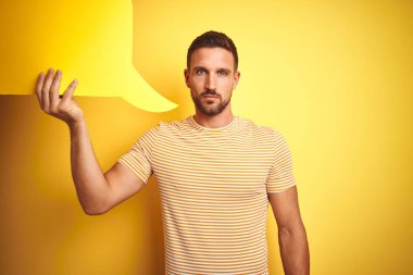 Genç adam ciddi düşünme akıllı yüz üzerinde kendine güvenen bir ifade ile sarı izole arka plan üzerinde mesaj için boş konuşma balonu tutan