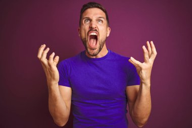 Lila izole arka plan deli ve deli bağırarak ve agresif ifade ve kollar kaldırdı ile bağırıyor üzerinde rahat mor t-shirt giyen genç adam. Hayal kırıklığı kavramı.