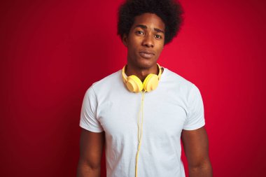 Genç afro-Amerikan adam yüzünde ciddi bir ifade ile izole kırmızı arka plan üzerinde kulaklık kullanarak müzik dinliyor. Kameraya basit ve doğal bir bakış.