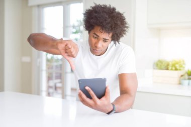 Afro-Amerikan adam kızgın yüz ile touchpad tablo kullanarak, başparmak aşağı, ret kavramı ile sevmediğimi gösteren negatif işareti
