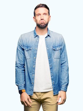 Komik surat ile yanakları şişirme denim ceket giyen sakal ve mavi gözlü yakışıklı adam. Ağız ile hava, deli ifade şişirilmiş.