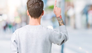 Genç yakışıklı adam giyen kazak izole üzerinde arka plan geriye doğru arkasında parmak eliyle işaret Posing