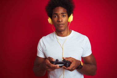 Afro oyun adam ciddi düşünme akıllı yüz üzerinde emin bir ifade ile izole kırmızı arka plan üzerinde joystick kulaklık kullanarak video oyunu oynuyor