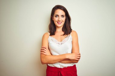 Beyaz izole arka plan üzerinde duran t-shirt giyen genç güzel kadın kamera bakarak çapraz kolları ile gülümseyen mutlu yüz. Pozitif kişi.