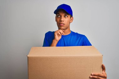 Genç yakışıklı arap teslimat adam izole beyaz arka plan üzerinde duran bir kutu tutan ciddi yüz soru hakkında düşünme, çok karışık bir fikir