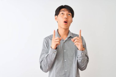 Izole beyaz arka plan üzerinde duran zarif gömlek giyen Çinli işadamı şaşırttı ve yukarı bakarak ve parmakları ile işaret ve kolları kaldırdı şaşırttı.