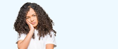Kıvırcık saçlı Genç güzel kadın beyaz t-shirt düşünme yorgun ve çapraz silah ile depresyon sorunları ile sıkılmış görünümlü giyiyor.
