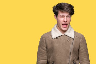 Genç yakışıklı adam izole arka plan üzerinde kış ceket giyen seksi ifade, neşeli ve mutlu yüz ile kameraya bakarak göz kırpma.