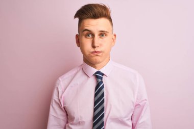 Genç yakışıklı işadamı komik yüzü ile izole pembe arka plan şişme yanakları üzerinde duran gömlek ve kravat giyiyor. Ağız hava ile şişirilmiş, deli ifade.