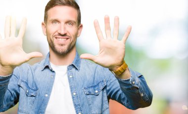 Mavi gözlü ve sakal gösteren ve parmak sayısı on ile işaret eden kot ceket giyen yakışıklı adam emin ve mutlu gülümseyen.