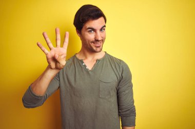 Sarı arka plan üzerinde duran rahat tişört giyen genç ve yakışıklı bir adam kendini beğenmiş ve mutlu bir şekilde gülümserken dört numarayı işaret ediyor..