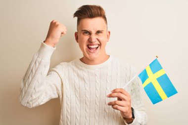 Izole beyaz arka plan üzerinde Sweadish İsveç bayrağı tutan genç yakışıklı adam kızgın ve öfke ile bağırarak sinirli, deli ve yükseltilmiş el ile bağırıyor, öfke kavramı