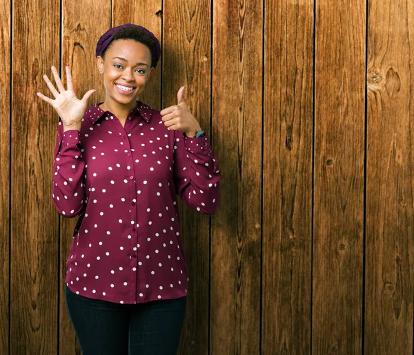 Beautiful young african american woman wearing head scarf over isolated background showing and pointing up with fingers number six while smiling confident and happy.