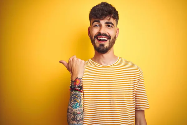Mladý Muž Tetováním Pruhovaným Tričkem Který Stojí Nad Izolovaným Žlutým — Stock fotografie
