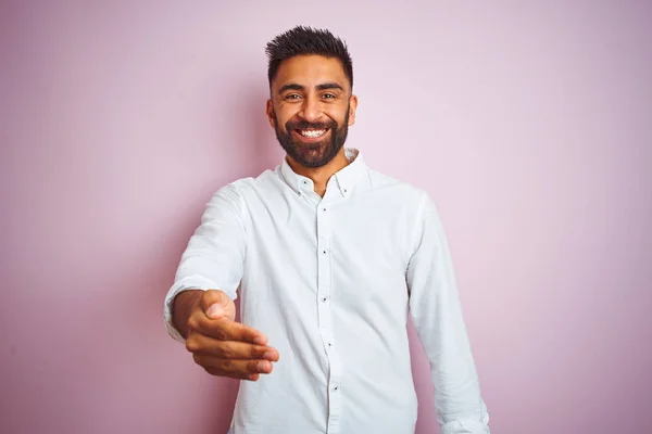 Young indian businessman wearing elegant shirt standing over isolated pink background smiling friendly offering handshake as greeting and welcoming. Successful business.