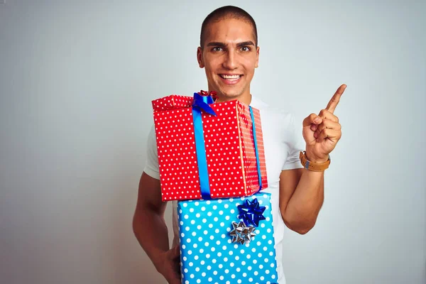 Young handsome man holding birthday gifts over white isolated background very happy pointing with hand and finger to the side