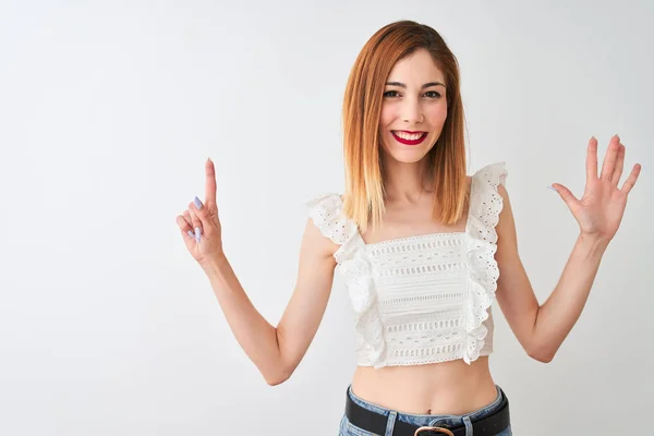 Beautiful redhead woman wearing casual t-shirt standing over isolated white background showing and pointing up with fingers number six while smiling confident and happy.
