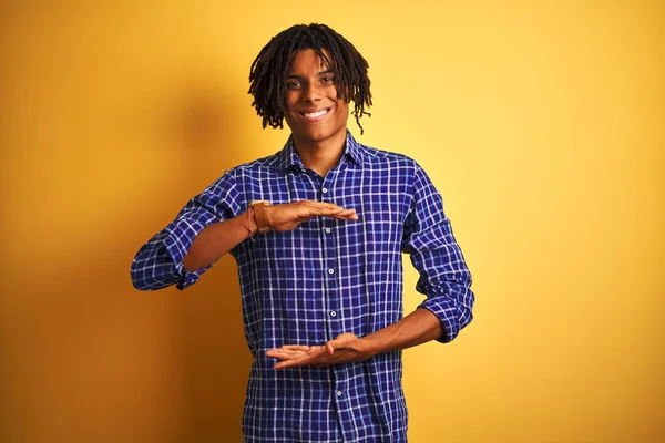 Büyük ve büyük boy işareti gösteren elleri ile izole sarı arka plan gesturing üzerinde duran rahat gömlek giyen dreadlocks ile Afro adam, ölçü sembolü. Kameraya bakarak gülümsüyor. Ölçme kavramı.