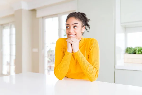 Beautiful african american woman with afro hair wearing a casual yellow sweater laughing nervous and excited with hands on chin looking to the side
