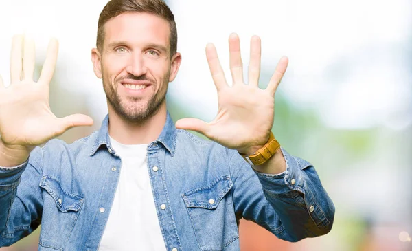 Mavi gözlü ve sakal gösteren ve parmak sayısı on ile işaret eden kot ceket giyen yakışıklı adam emin ve mutlu gülümseyen.