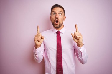 Pembe izole arka plan üzerinde kravat ve zarif gömlek giyen iş adamı şaşırttı ve yukarı bakarak ve parmakları ile işaret ve kolları kaldırdı şaşırttı.