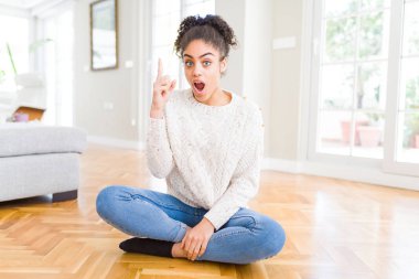 Afro saçlı güzel genç Afrikalı Amerikalı kadın yerde oturan başarılı bir fikir ile parmak yukarı işaret. Çıkıldı ve mutlu. Bir numara.