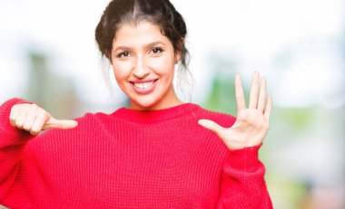 Genç güzel kadın kırmızı kazak ve topuz gösteren giyen ve parmak numarası altı ile işaret ederken emin ve mutlu gülümseyen.