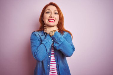 Denim gömlek giyen güzel kızıl saçlı kadın ve izole pembe arka plan üzerinde çizgili t-shirt bağırarak boğulma kısık çünkü acı boğmak. Sağlık sorunu. Boğulma ve intihar kavramı.