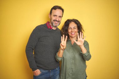 Izole sarı arka plan üzerinde Güzel orta yaş çift gösteren ve parmakları ile işaret ederken emin ve mutlu gülümseyerek sekiz.