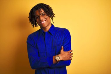 Izole sarı arka plan üzerinde mekanik üniforma giyen dreadlocks ile Afro işçi adam kameraya bakarak çapraz kolları ile gülümseyen mutlu yüz. Pozitif kişi.