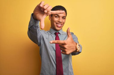 Genç yakışıklı Arap işadamı gömlek giyen ve izole sarı arka plan üzerinde kravat mutlu yüzü ile elleri ve parmakları ile çerçeve yapma gülümseyerek. Yaratıcılık ve fotoğrafçılık konsepti.