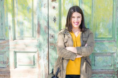 Güneşli bir günde şehir sokakta yürürken duvardaki, kendinden emin ve neşeli yaslanmış gülümseyen güzel genç kadın