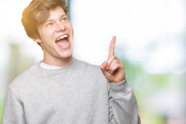Başarılı fikirle izole arka plan işaret parmağı üzerinde sweatshirt giyen genç yakışıklı sportif adam. Çıktıktan ve mutlu. Bir numara.