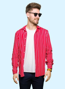 Genç yakışıklı uzak tarafına yüzünde, doğal ifade gülümseme ile seyir giyen güneş gözlüğü adam. Kendine güvenen gülüyor.