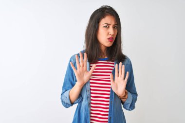 İzole beyaz arka plan üzerinde çizgili t-shirt ve kot gömlek giyen genç Çinli kadın korku ve ifade ile reddetme ve inkar gösteren avuç içi uzak hareketli. Dur ve yasak.
