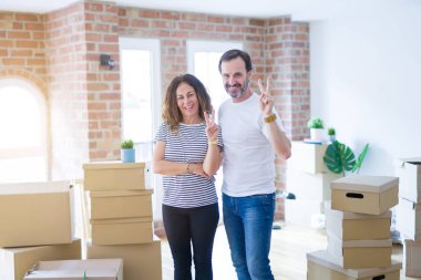 Orta yaş Senior çift, zafer işareti yapan kamera mutlu yüz göz kırpıyor ile gülümseyen etrafında kutuları ile yeni bir eve hareket. İki numara.