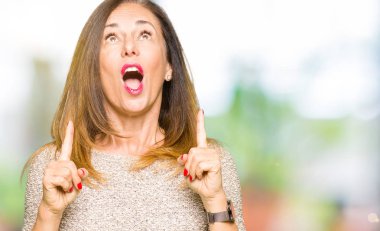 Moda kazak giyen güzel orta yaş kadın hayrete ve yukarıya bakıyor ve parmakları ile işaret ve silah kaldırdı şaşırttı.