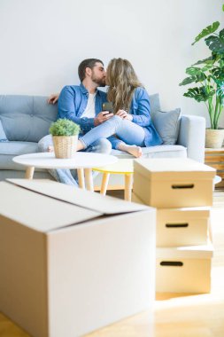 Yeni bir eve hareket akıllı telefon kullanarak kanepede oturan aşk sarılma genç çift